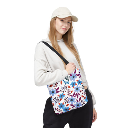 Young person wearing a light hoodie and cap carries a Floral Tote Bag, featuring a vibrant blue and purple blossom pattern, ideal for summer outings, embodying FireBrook Essentials' cheerful, uplifting design ethos.