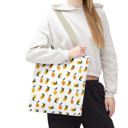 Casually dressed person holds the Lemon Drop Toss Tote Bag, showcasing its vibrant lemon and leaf pattern. Perfect for brightening summer outings with FireBrook Designs' signature cheerful and practical style.