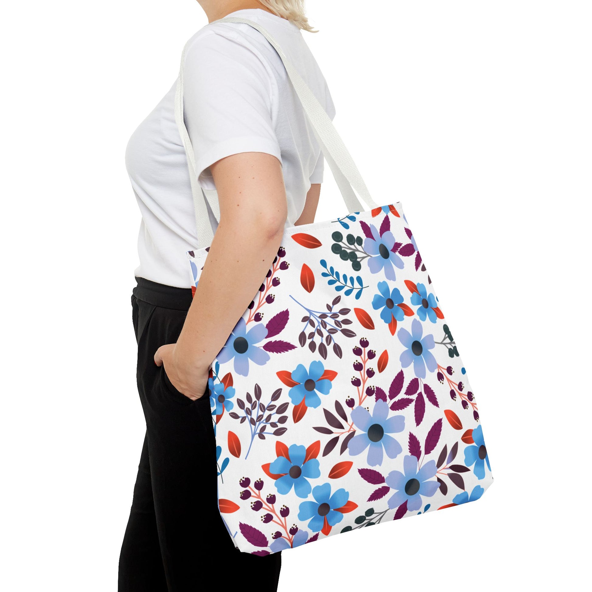 Floral Tote Bag carried over the shoulder, featuring a vibrant pattern with blue, lavender flowers, deep purple leaves, and red accents. A stylish, durable accessory from FireBrook Essentials for joyful outings.