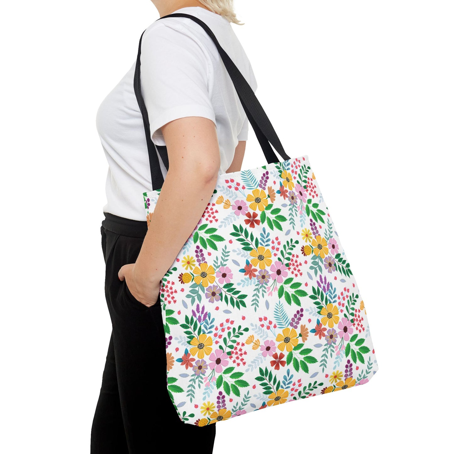 Person carrying the Floral Tote Bag over the shoulder, featuring vibrant clusters of flowers and green leaves on a white background, complemented by black straps, ideal for brightening summer outings.