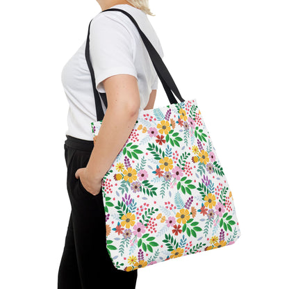 Person carrying the Floral Tote Bag over the shoulder, featuring vibrant clusters of flowers and green leaves on a white background, complemented by black straps, ideal for brightening summer outings.