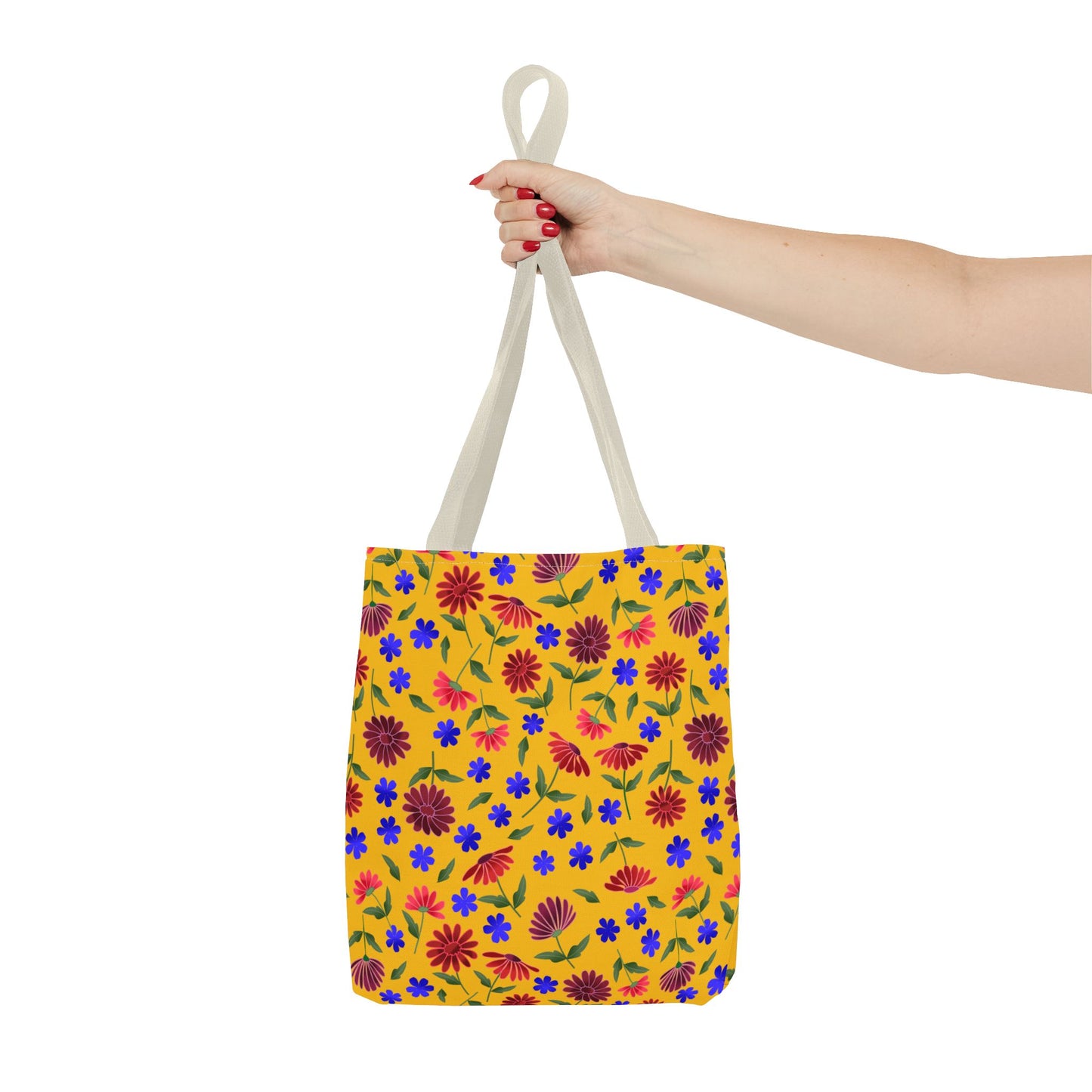 Golden Wildflower Tote Bag with vibrant red and burgundy daisies, small blue flowers, and green leaves on a yellow canvas, held by a hand with red nails, showcasing its lively design.
