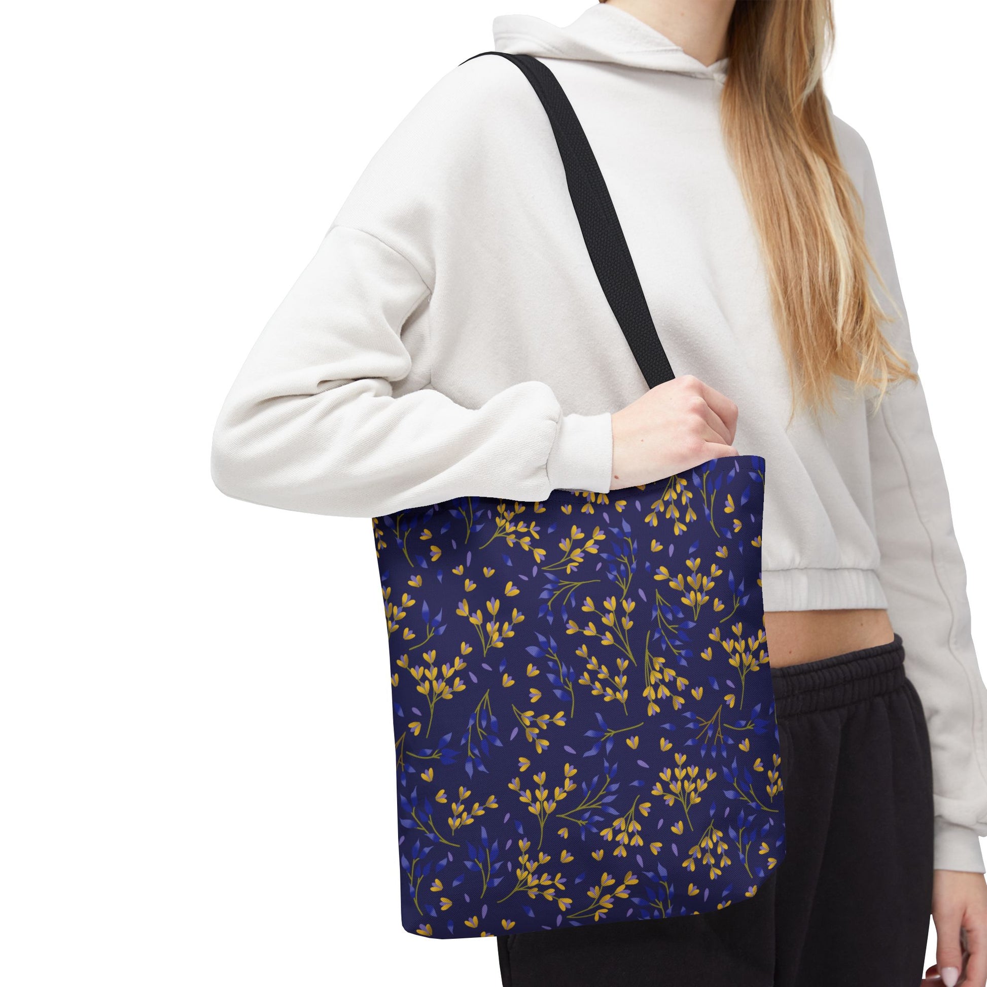 Floral Tote Bag with a dark navy-blue background featuring golden yellow and cobalt blue leafy sprigs. The bag, held over a shoulder, complements casual attire, embodying FireBrook Designs' cheerful and practical style.