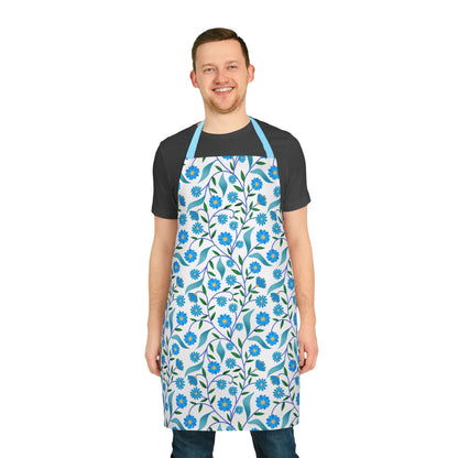 Man wearing Apron Floral Design with blue flowers and green leaves over a dark t-shirt and jeans. This stylish, stain-free apron from FireBrook Designs combines comfort and vibrant patterns, perfect for any kitchen activity.