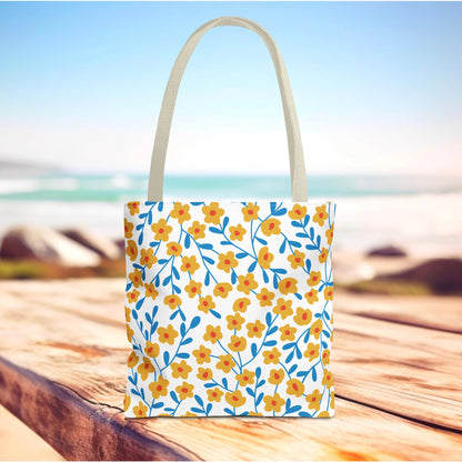 Floral Tote Bag featuring a vibrant pattern of yellow-orange flowers and blue leaves, displayed on a beach boardwalk, highlighting durable polyester and reinforced handles—perfect for joyful summer outings.