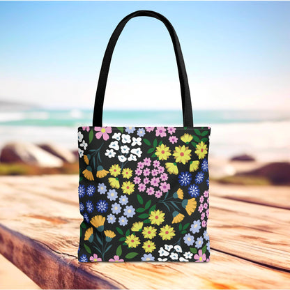 Floral Tote Bag with black straps on a rustic wooden surface, featuring a vibrant floral pattern with various blossoms, ideal for summer outings, aligning with FireBrook Designs' uplifting and joyful style.