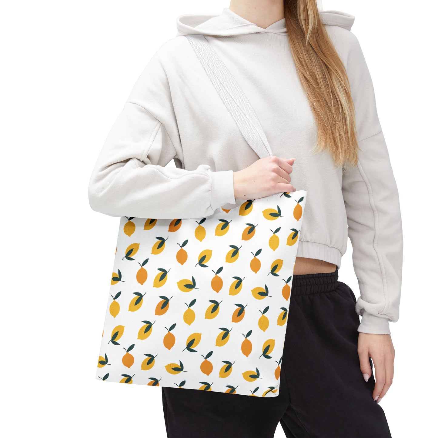 The Lemon Drop Toss Tote Bag, adorned with vibrant lemon motifs, is showcased on a person wearing casual attire. This stylish tote embodies FireBrook Designs' cheerful and uplifting aesthetic, perfect for joyful outings.