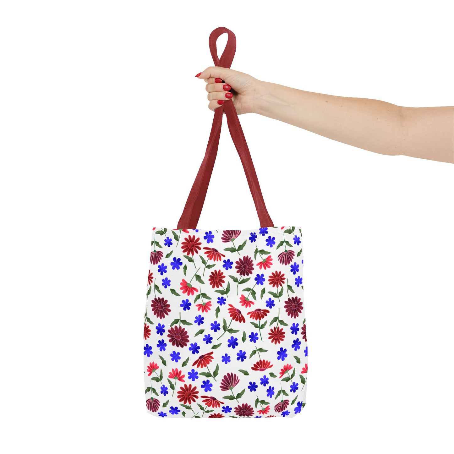 Floral Pattern Tote Bag — Red & Blue Wildflower All-Over Print held by red-nailed hand, showcasing vibrant floral design. Burgundy straps and durable black stitching highlight its cheerful, versatile style.