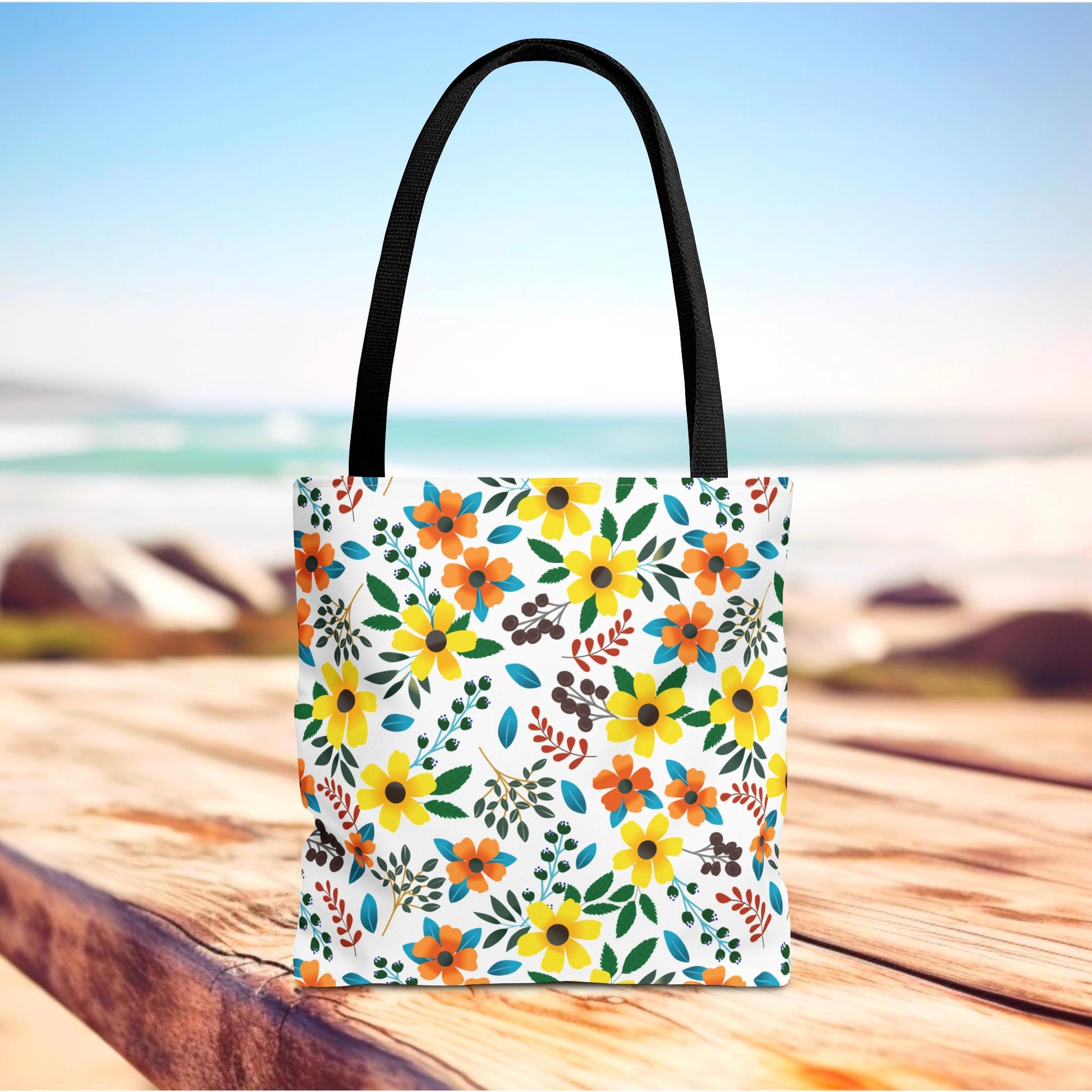 Sunny Meadow Mix Tote Bag on wooden surface, featuring vibrant yellow and orange floral pattern. Ideal for summer outings, with durable polyester, reinforced black handles, and boxed corners for extra space.