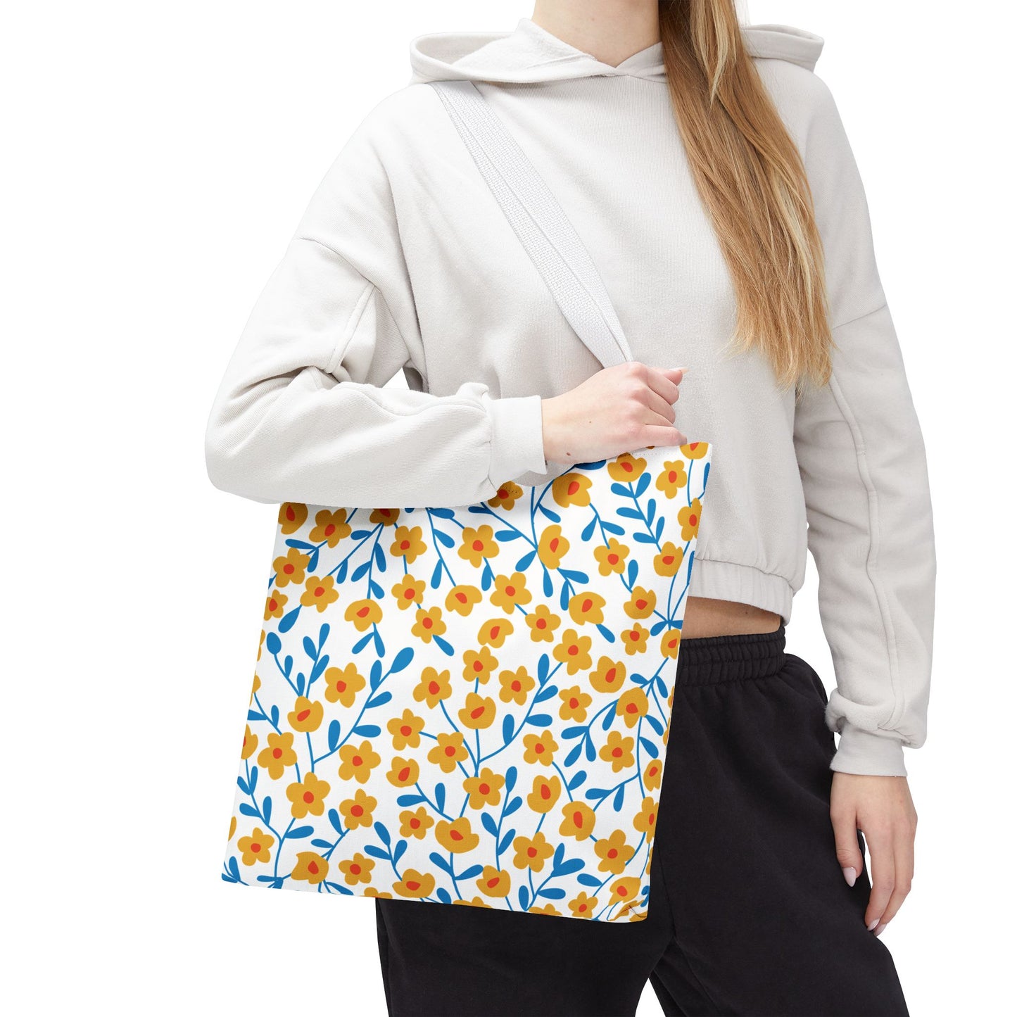 Buttercup Cream Tote Bag featuring a playful pattern of yellow flowers with red centers and blue stems, showcased over a shoulder. Perfect for summer, blending durability with vibrant, cheerful design.