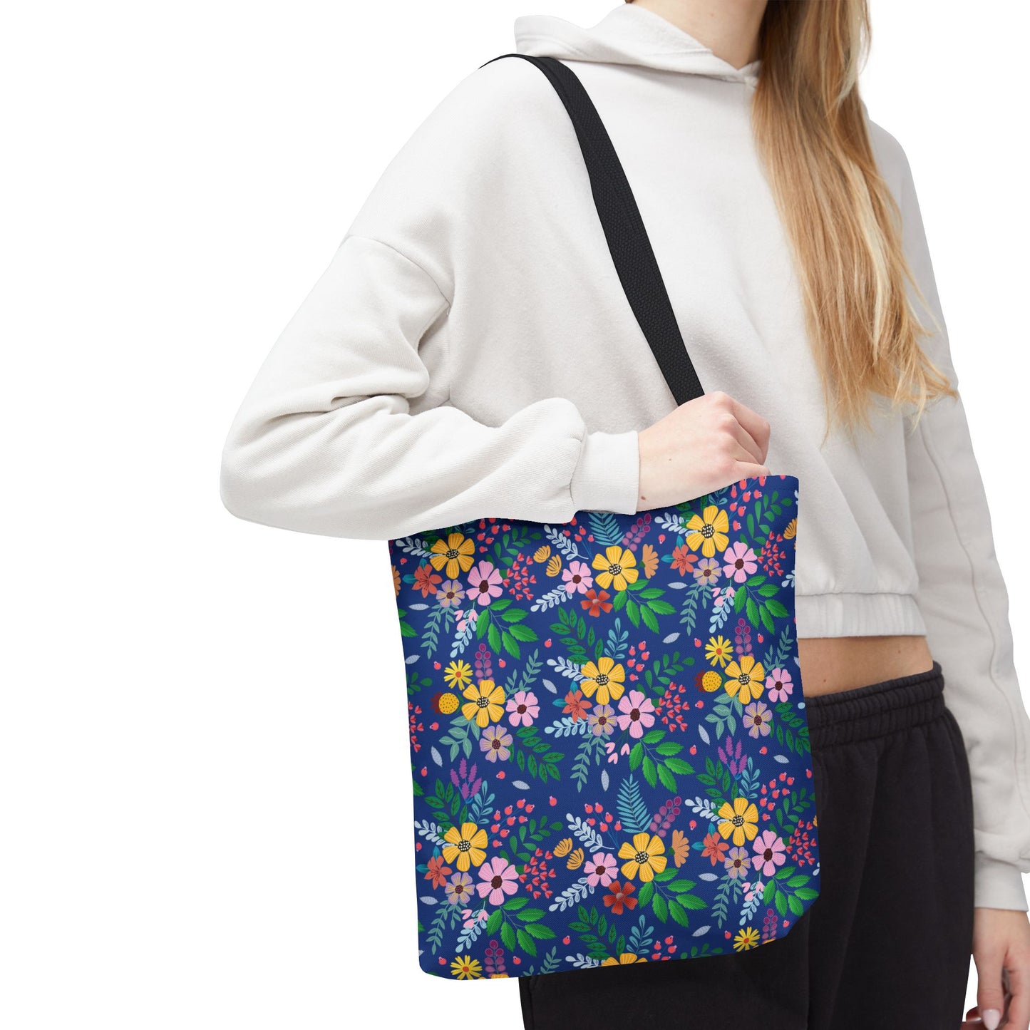 A person wears a light-colored cropped hoodie and carries a Floral Tote Bag with a dark blue background and vibrant floral pattern, perfect for summer outings and enhancing joyful, stylish living.