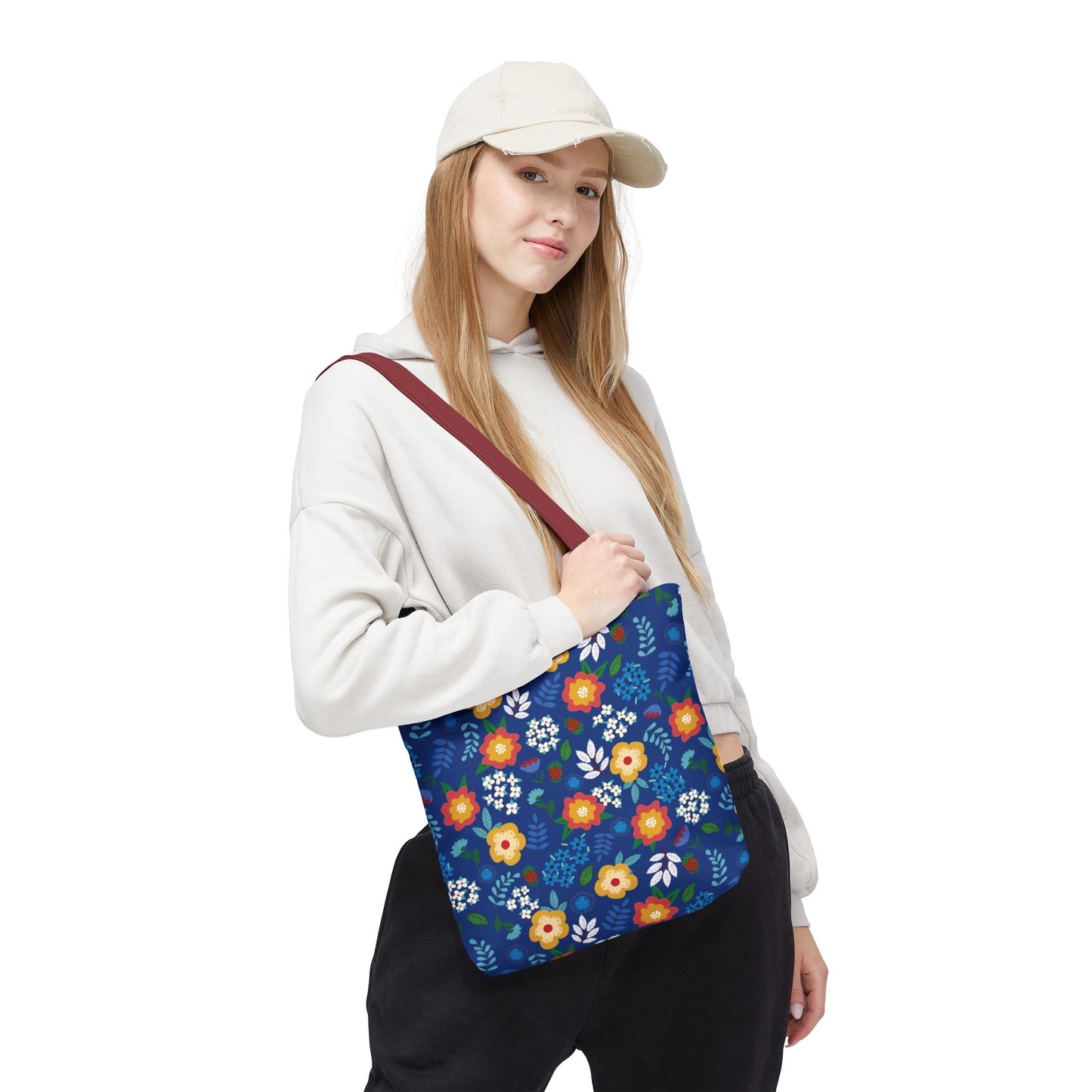 Floral Tote Bag carried by a casually dressed person, featuring a deep blue background with vibrant floral patterns in yellow, orange, and white, and a contrasting reddish-brown strap, perfect for cheerful summer outings.