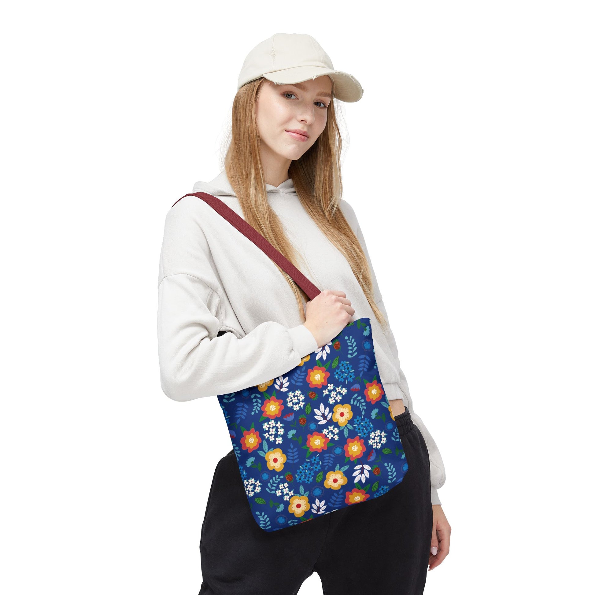 Floral Tote Bag carried by a casually dressed person, featuring a deep blue background with vibrant floral patterns in yellow, orange, and white, and a contrasting reddish-brown strap, perfect for cheerful summer outings.