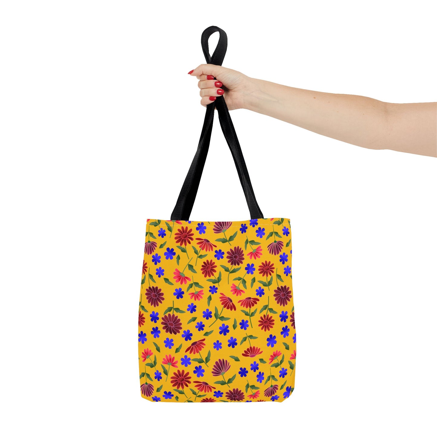 Golden Wildflower Tote Bag held by black handles, showcasing a vibrant floral pattern with red and purple daisies, blue flowers, and green leaves on a bright yellow background, emphasizing cheerful, practical design.