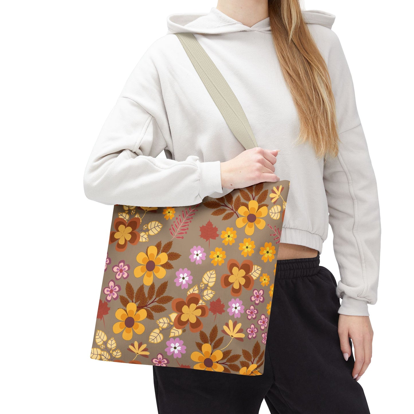 Person wearing a light-colored hoodie and dark pants carries the Harvest Brown Bloom Tote Bag, featuring a retro floral pattern in orange, yellow, brown, pink, and yellow, against a tan-brown background.
