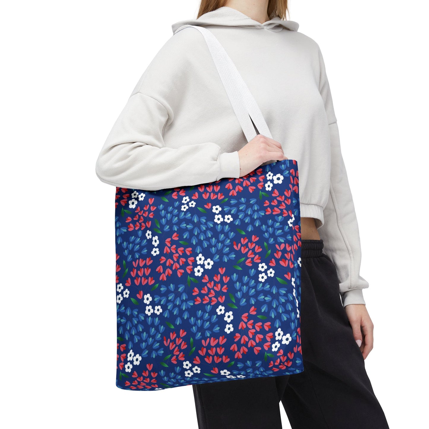 The Berry Blue Festival Tote Bag, adorned with vibrant red, light-blue, and white floral patterns against a navy backdrop, features white straps, ideal for summer outings, embodying FireBrook Essentials' joyful, uplifting design ethos.
