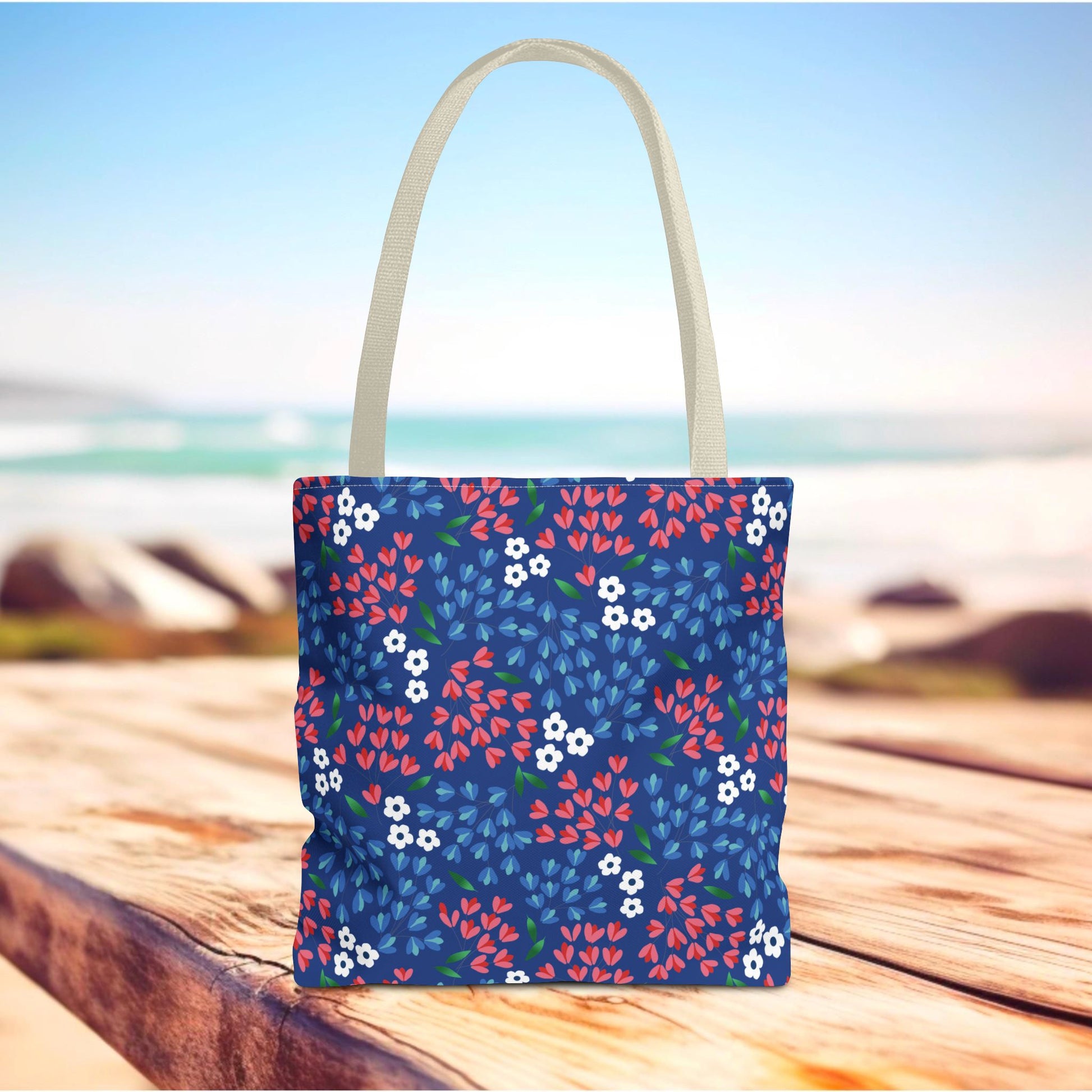 Floral Tote Bag featuring a deep blue body adorned with red and blue blossoms, set against a beach backdrop. Ideal for summer outings, reflecting FireBrook Designs' joyful, stylish ethos.