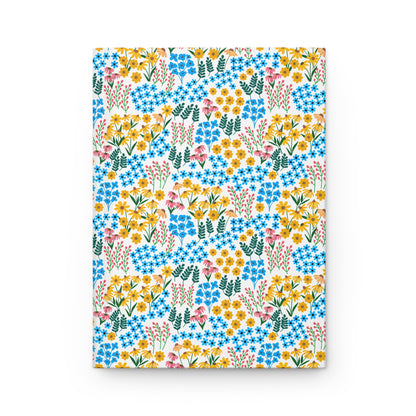 HARDCOVER JOURNAL, MATTE, RULED, 5X7, SEWN BIND, CLEAN-TEAR PAGES – WILDFLOWER MEADOW MIX features a durable matte cover with a vibrant floral pattern of daisies, blue blossoms, pink spikes, and green leaves.