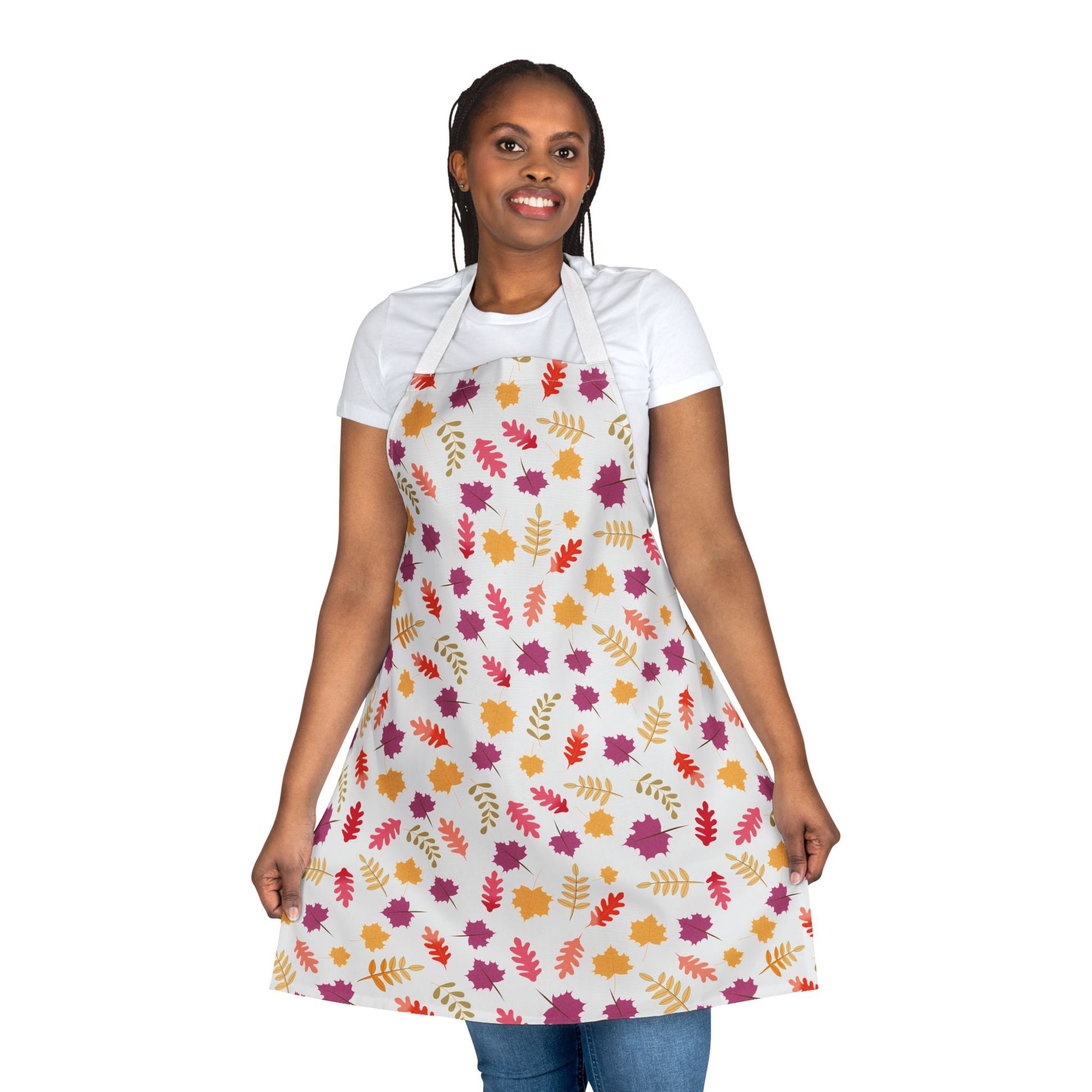 Woman wearing FireBrook Designs Apron Floral Design, featuring a vibrant leaf motif on a light canvas, smiling and holding apron sides, paired with casual blue jeans; ideal for joyful, stylish home activities.