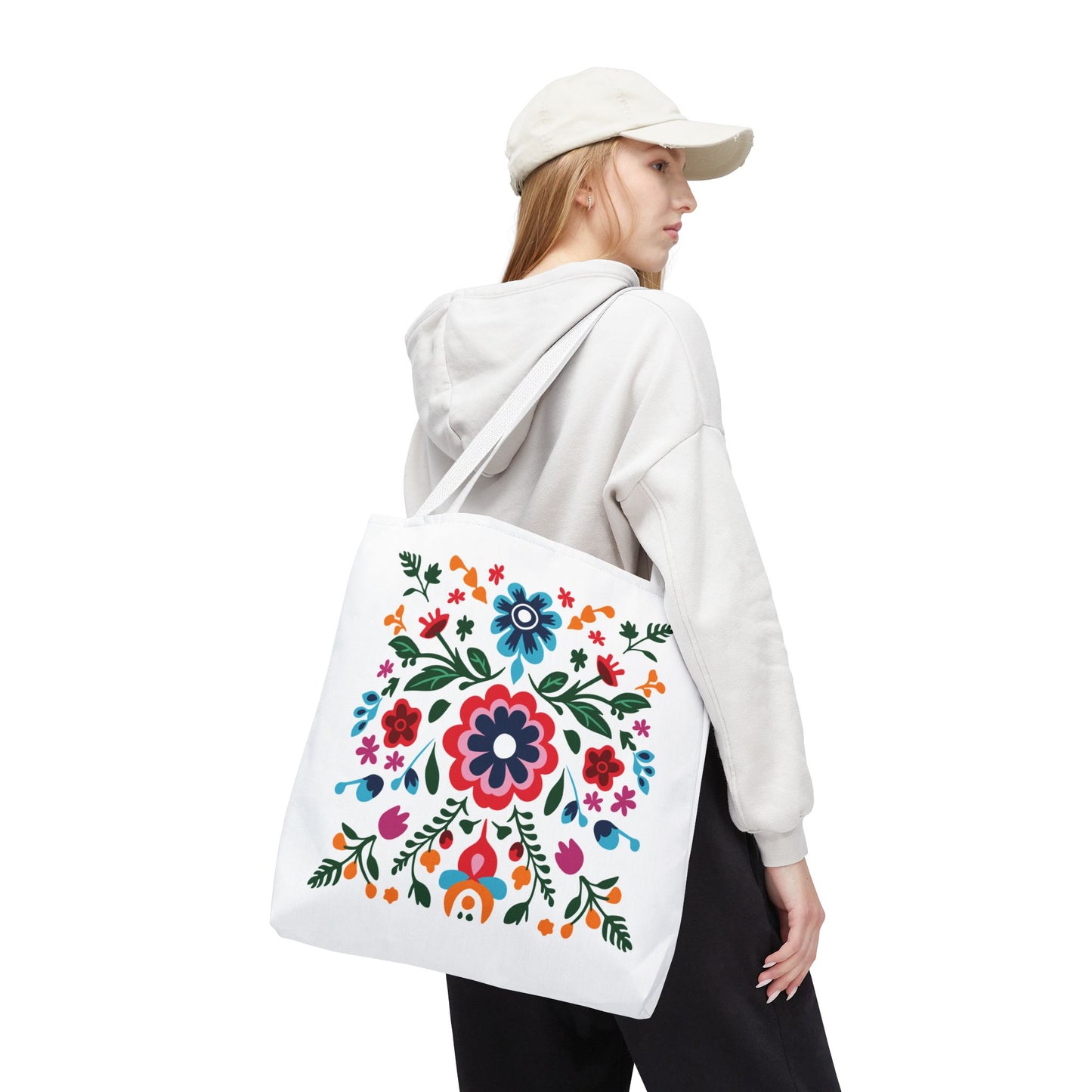 Woman wearing a floral sweatshirt and white hat carries a Floral Tote Bag adorned with colorful flowers, showcasing FireBrook Essentials' blend of style and practicality.