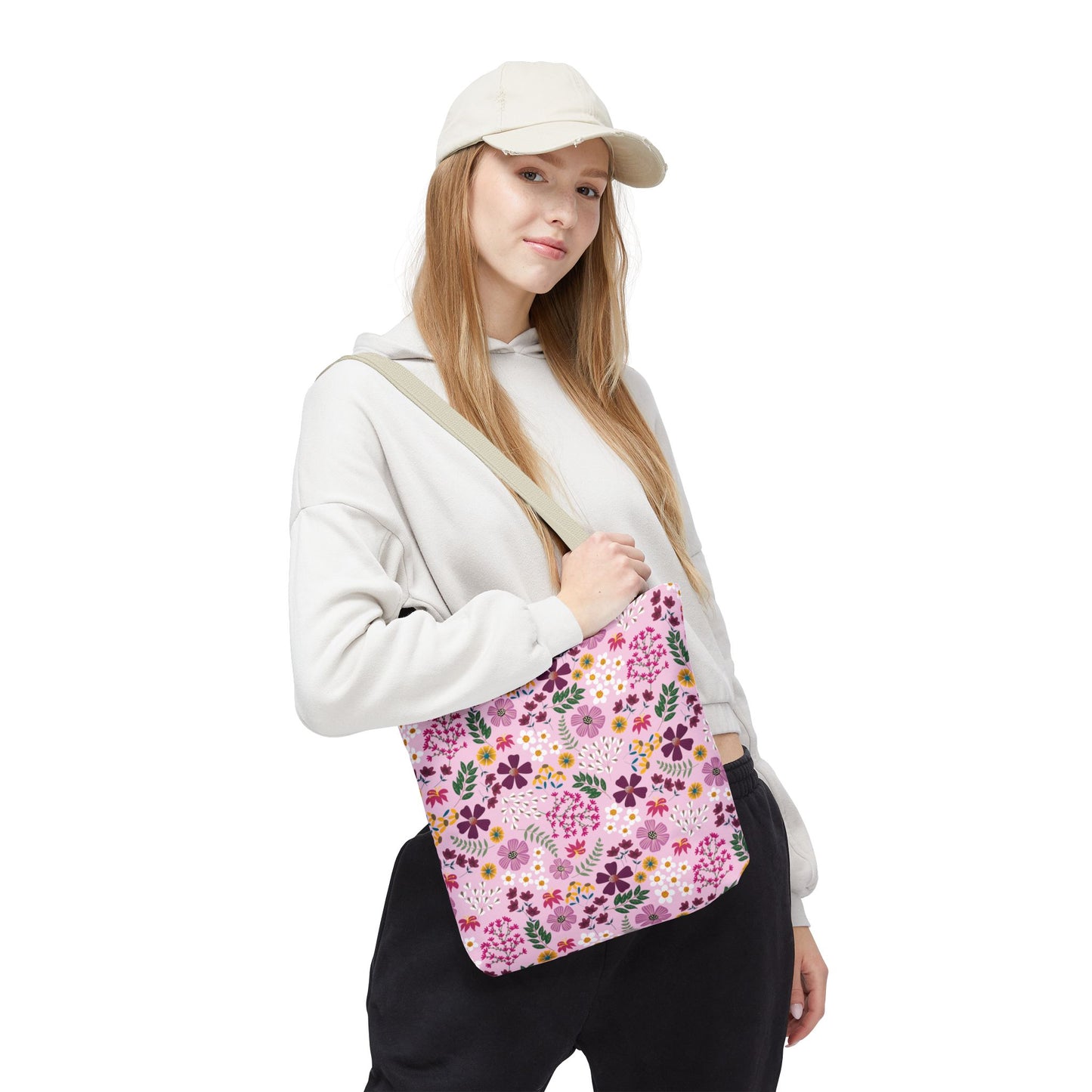 Young woman wearing a light-colored baseball cap, pale hoodie, and dark pants, carries the Rose Garden Blush Tote Bag with a pink floral pattern, showcasing FireBrook Designs' stylish, durable everyday accessory.