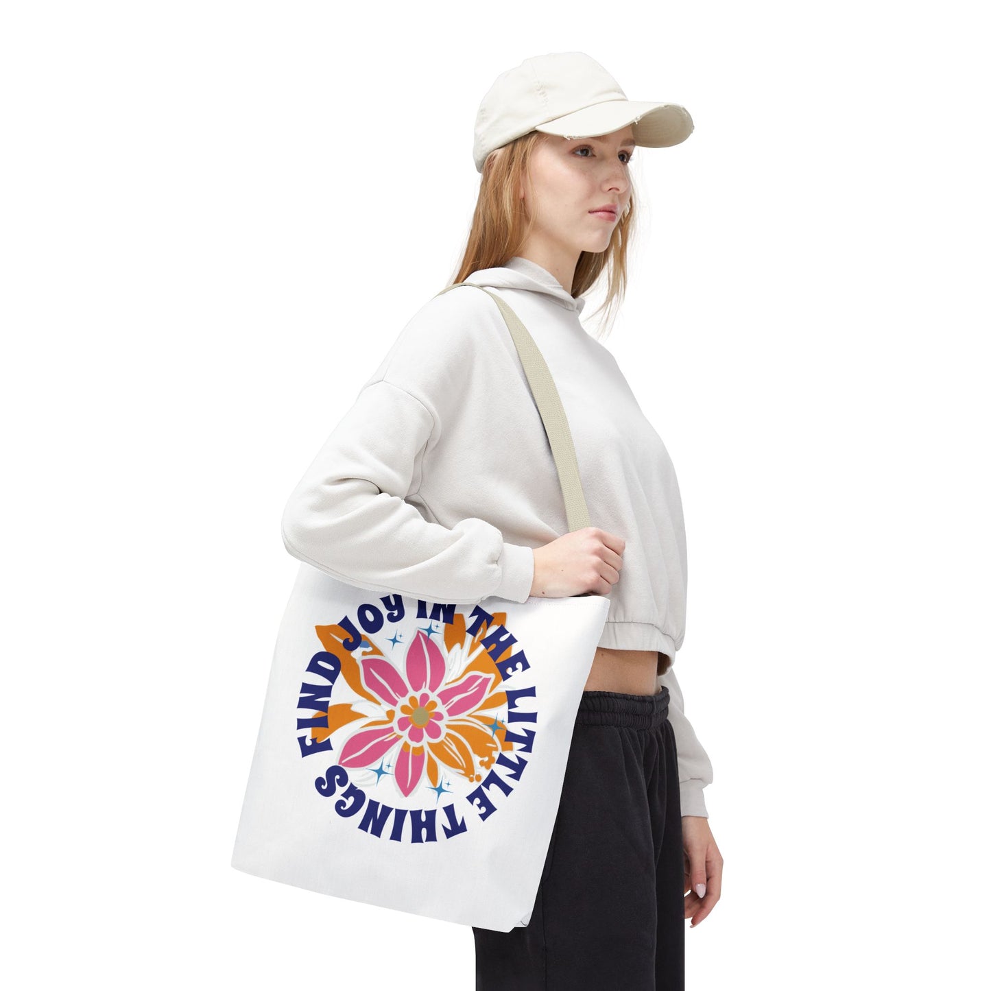 Find Joy in Little Things Tote Bag held by a woman in a white hat and sweatshirt, featuring a flower design, perfect for spreading positivity.