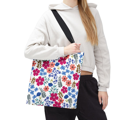 Person wearing a light cropped hoodie and dark pants carries a Floral Tote Bag over their shoulder. The bag features vibrant pink, red, and blue flowers, embodying FireBrook Essentials' cheerful and uplifting design ethos.