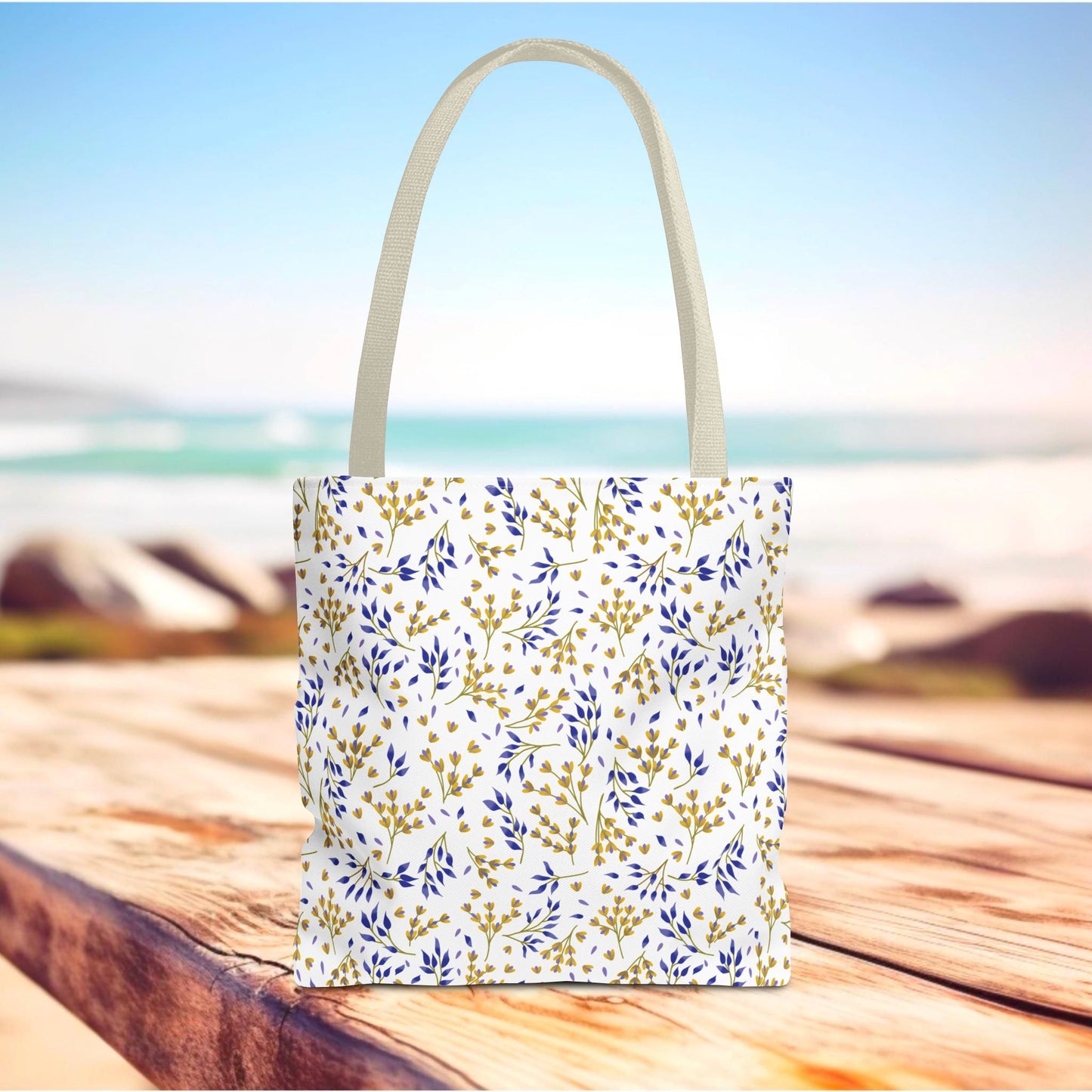 Wild Herb Garden Tote Bag on a boardwalk, featuring a white body with gold-yellow and deep blue leaf pattern, off-white handles, perfect for summer outings and beach trips.