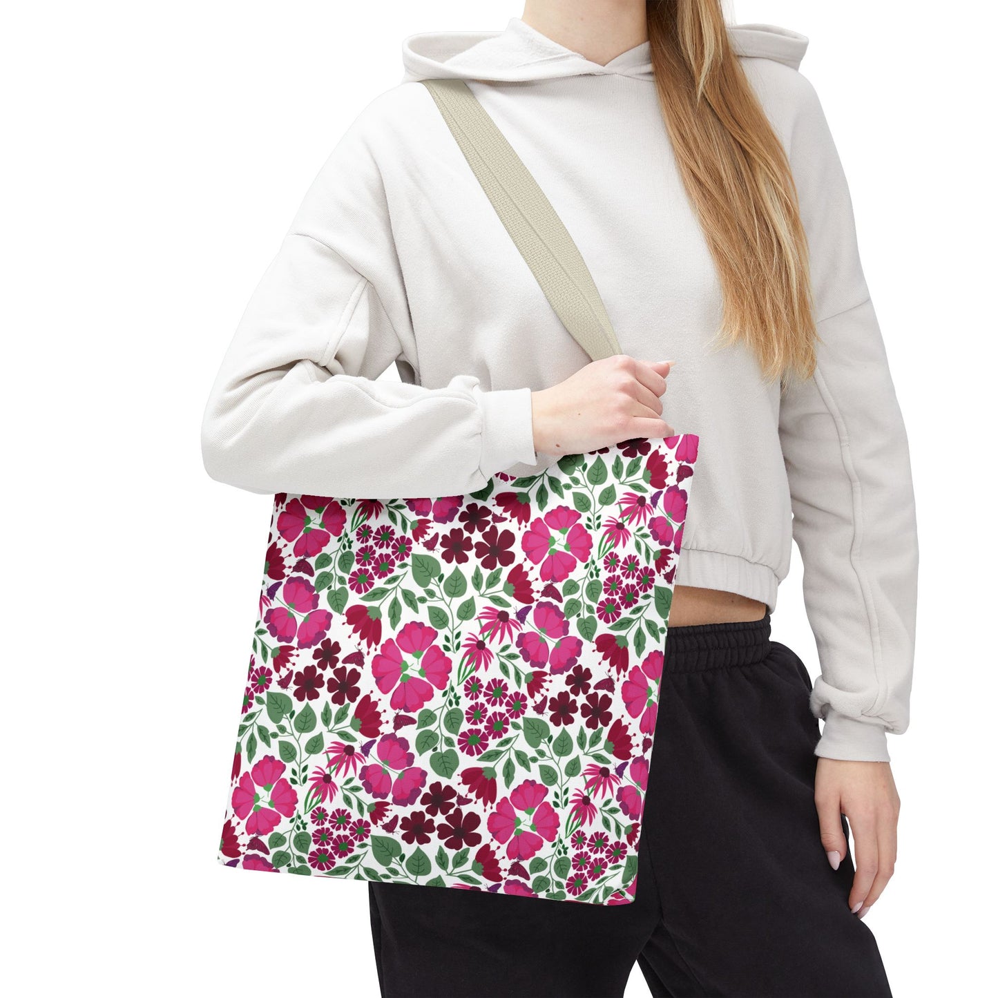 Pink Lady Tote Bag features a vibrant pink, burgundy, and green floral pattern on white, carried by a person in a light hoodie. Ideal for adding color and joy to everyday outfits.