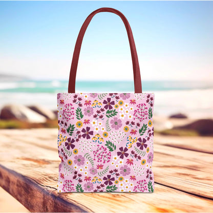 Floral Tote Bag with a pink base and vibrant blossoms, featuring burgundy handles, rests on a wooden surface. Ideal for daily essentials, it embodies FireBrook Designs' commitment to stylish, durable solutions.