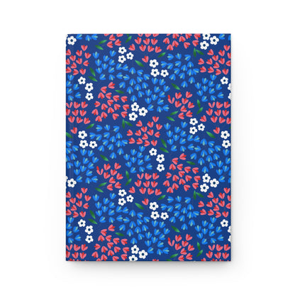 HARDCOVER JOURNAL, MATTE, RULED, 5X7, SEWN BIND, CLEAN-TEAR PAGES – WILDFLOWER SKY features a navy cover with vibrant coral, sky-blue petals, white flowers, and green leaves in a seamless floral pattern.