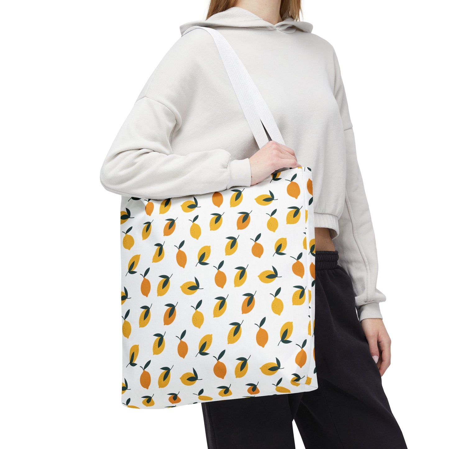 Person holds the Lemon Drop Toss Tote Bag, showcasing a lively pattern of stylized lemons. Ideal for summer outings, this durable bag from FireBrook Designs adds a vibrant touch to any outfit.