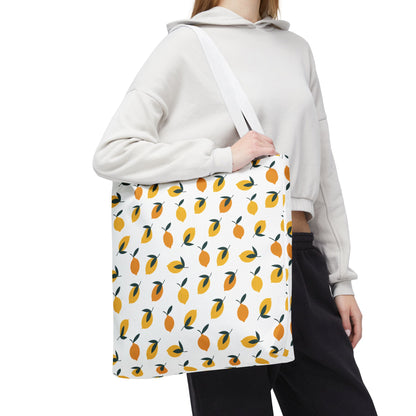 Person holds the Lemon Drop Toss Tote Bag, showcasing a lively pattern of stylized lemons. Ideal for summer outings, this durable bag from FireBrook Designs adds a vibrant touch to any outfit.