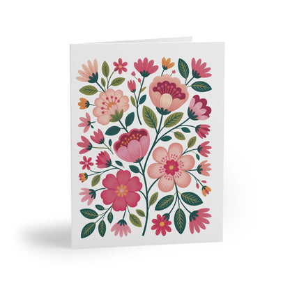 Flower Greeting Cards — Pack of 8/16/24, featuring a vibrant floral pattern in pink and peach with dark-green leaves, stand elegantly folded, ready to brighten any occasion with cheerful charm.