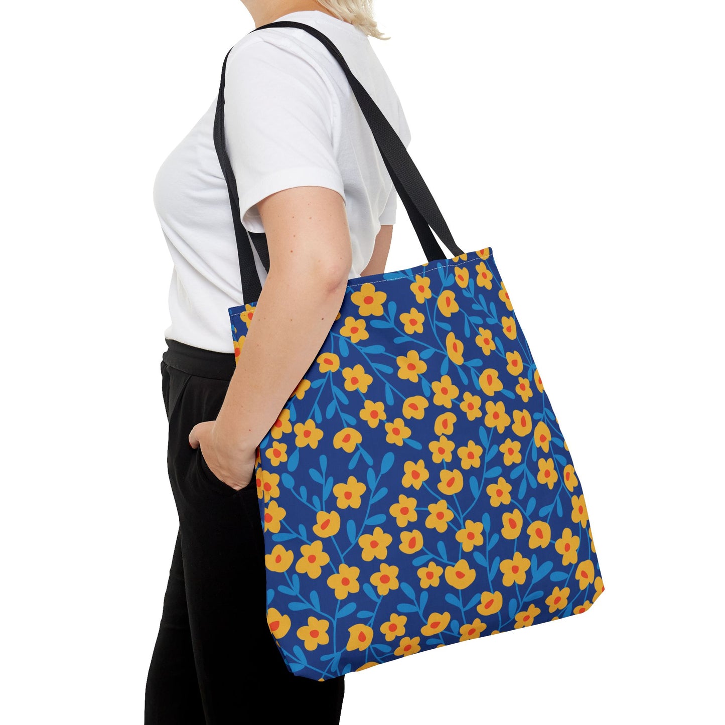 Person wearing a white t-shirt and black pants, carrying a Cobalt Poppy Field Tote Bag with a bright blue background and yellow floral pattern, featuring black straps over their shoulder.