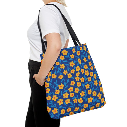 Person wearing a white t-shirt and black pants, carrying a Cobalt Poppy Field Tote Bag with a bright blue background and yellow floral pattern, featuring black straps over their shoulder.