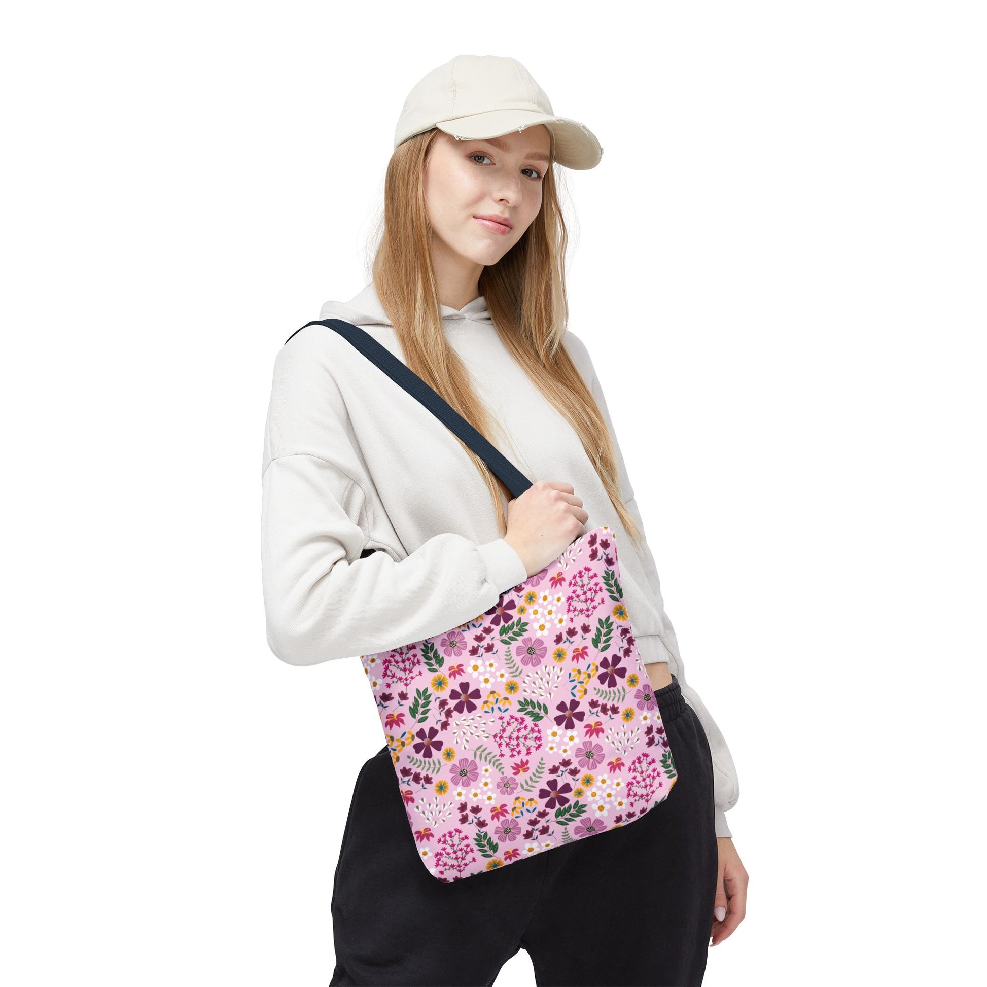 Young woman models the Floral Tote Bag, featuring a pink background with purple, yellow, and white flowers, showcasing its stylish, durable design ideal for everyday use from FireBrook Designs.