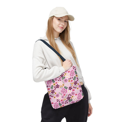 Young woman models the Floral Tote Bag, featuring a pink background with purple, yellow, and white flowers, showcasing its stylish, durable design ideal for everyday use from FireBrook Designs.