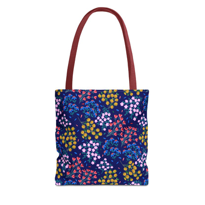 Midnight Garden Tote Bag showcases a dark navy-blue body with a vibrant floral pattern, featuring clusters of blooms in various colors. It has sturdy, flat shoulder straps in reddish-maroon.