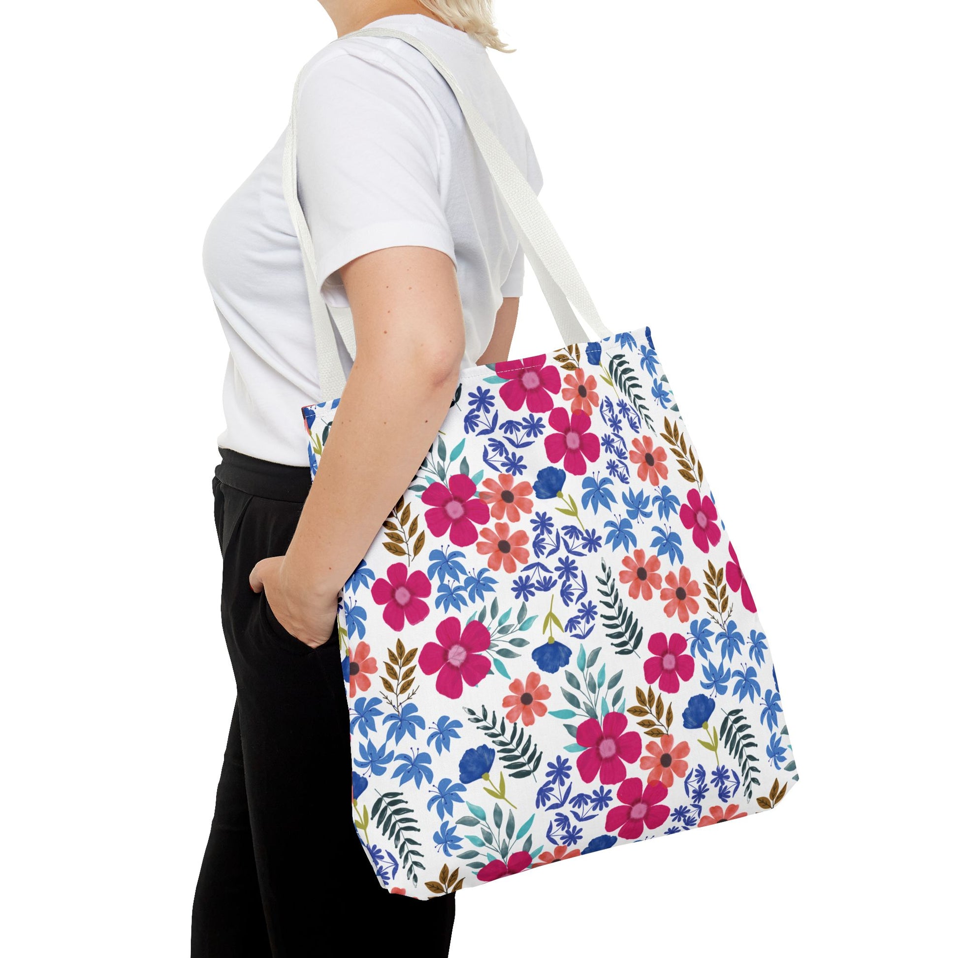 Floral Tote Bag with a vibrant hand-painted floral pattern in pinks and blues, carried over the shoulder by a person. Ideal for brightening summer outings, featuring durable polyester and reinforced handles.