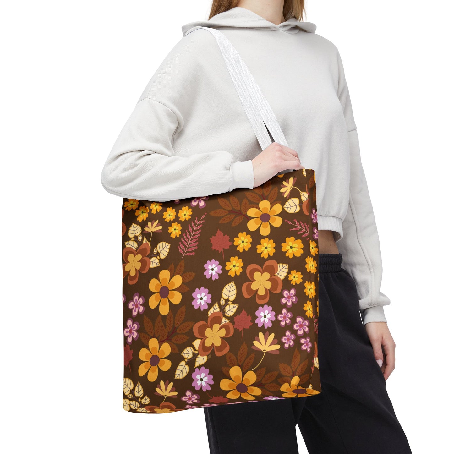 Floral Tote Bag featuring a retro-style pattern with orange, yellow, and pale pink flowers on a rich brown background, carried over the shoulder with white webbing straps. Perfect for summer outings.