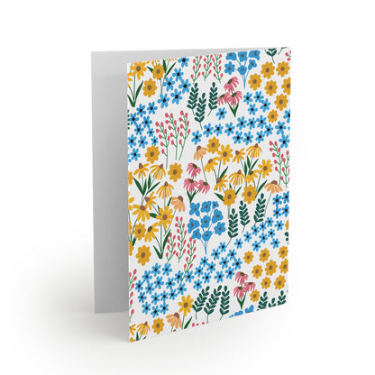 Floral Greeting Cards — Pack of 8/16/24, featuring a vibrant, hand-drawn floral pattern of blue, yellow, and pink flowers with green leaves on a white background. Cards are folded, matte-finished, and include matching envelopes.