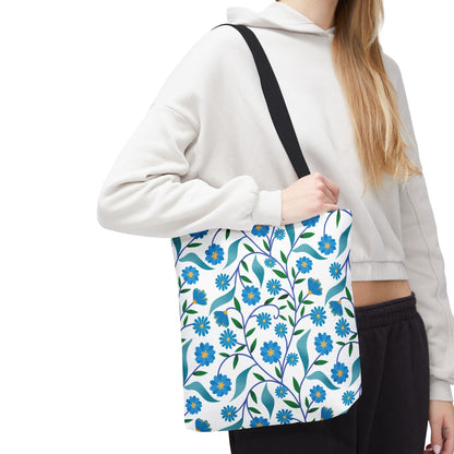 Person wearing a light hoodie and dark pants carries a Blue Floral Tote Bag featuring stylized blue flowers and green leaves with a black strap, embodying FireBrook Designs' cheerful, uplifting style.