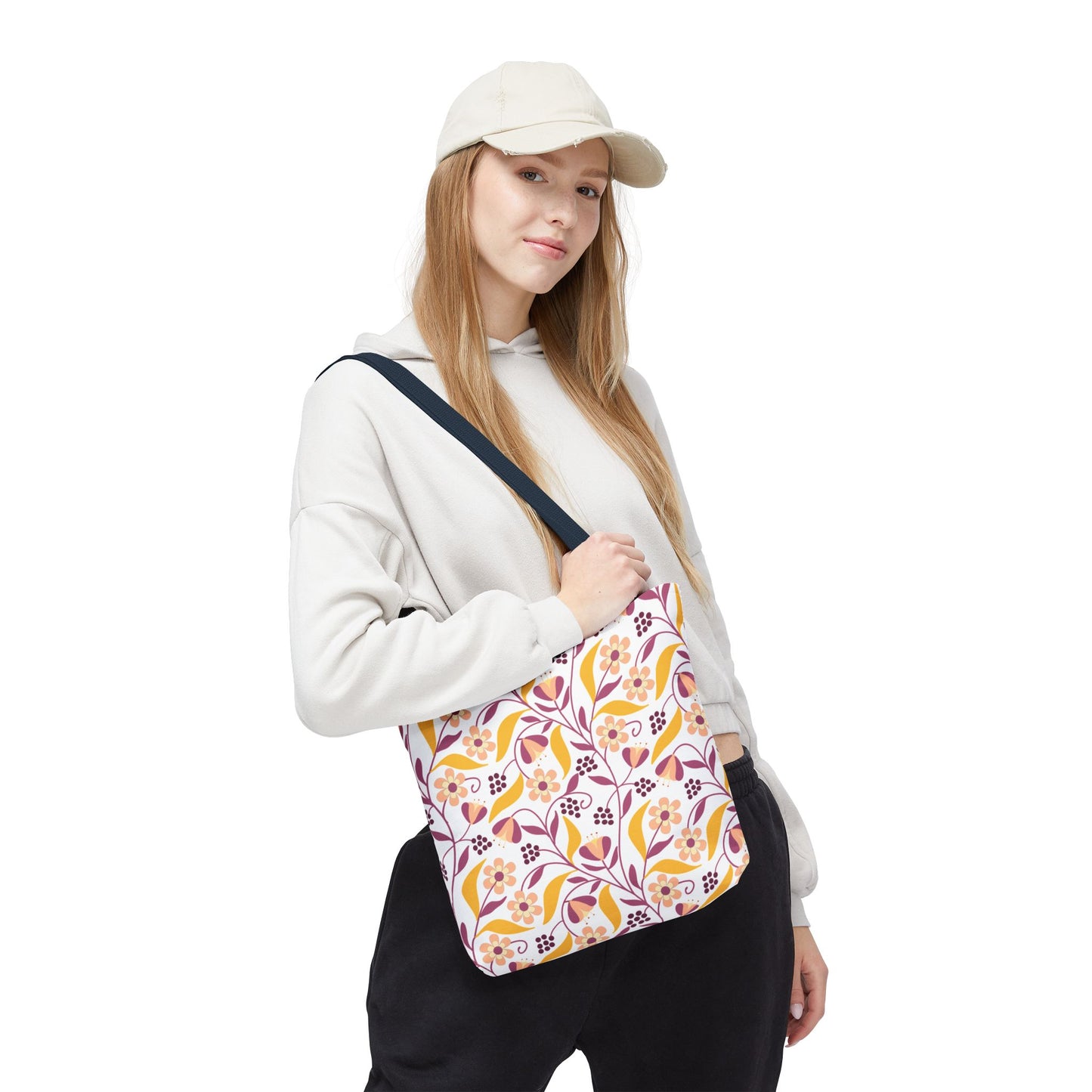 Model wearing a light-beige cap and hoodie with dark pants, showcasing the Golden Paisley Floral Tote Bag. The bag features vibrant floral patterns and a navy strap, embodying FireBrook Designs' joyful and uplifting style.