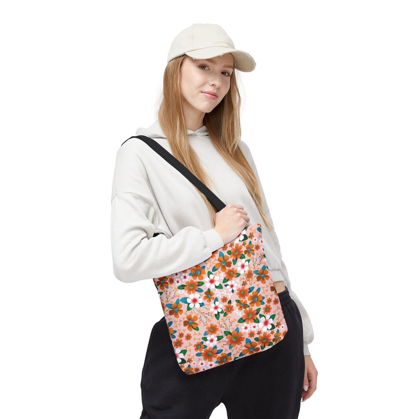 Woman wearing light hoodie and baseball cap carries the Peach Poppy Grove Tote Bag, adorned with vibrant orange, green, and white floral print. Ideal for summer outings, this tote embodies FireBrook Designs' cheerful and joyful spirit.