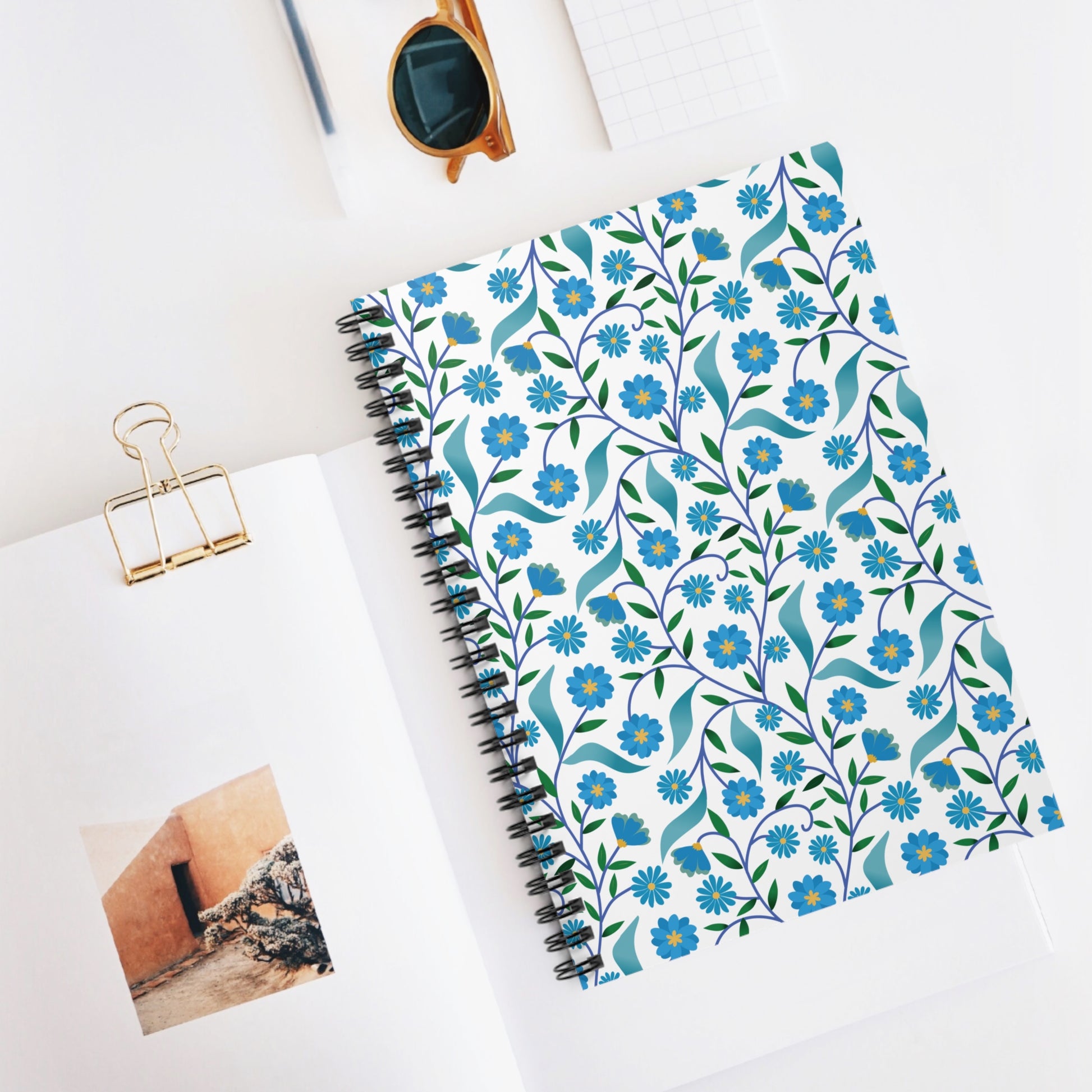 Floral Spiral Notebook with vibrant floral design on a white cover, central to a stylish workspace. Ideal for creativity and organization, it embodies FireBrook Designs' uplifting touch.