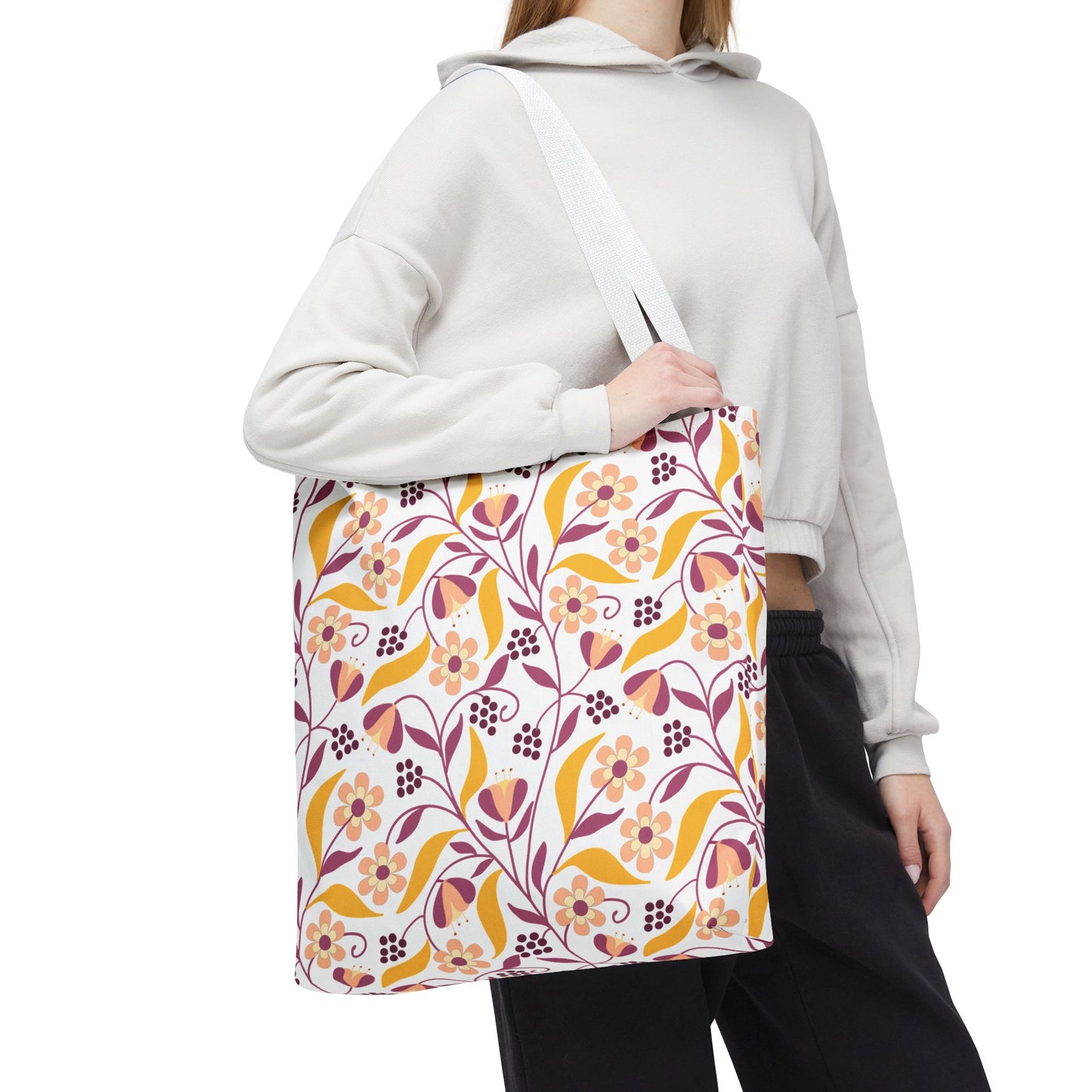 Floral Tote Bag displayed: a canvas tote with a vibrant floral-and-leaf pattern in orange, mustard yellow, and mauve, worn over light-colored hoodie, embodying FireBrook Designs' uplifting style for joyful outings.