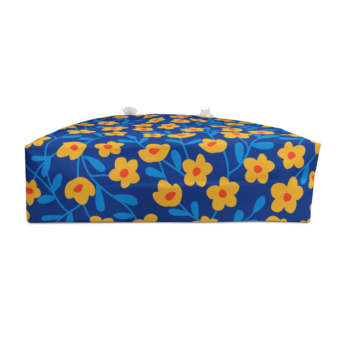 Weekender Bag displayed as a low, rectangular floor cushion adorned with bright floral fabric, featuring stylized yellow flowers. Includes fabric tie-strings with tassels, embodying FireBrook Designs' joyful and stylish essence.