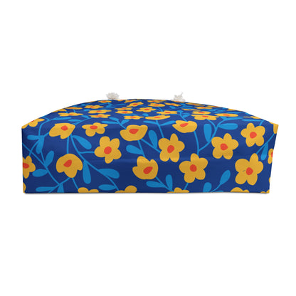 Weekender Bag displayed as a low, rectangular floor cushion adorned with bright floral fabric, featuring stylized yellow flowers. Includes fabric tie-strings with tassels, embodying FireBrook Designs' joyful and stylish essence.