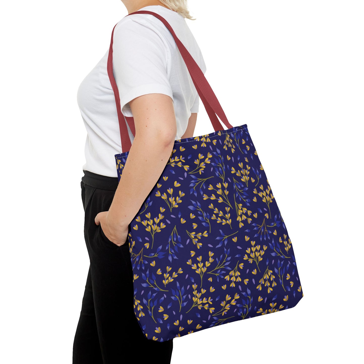 A person carries a Floral Tote Bag with burgundy-red straps and a navy-blue body adorned with yellow and blue botanical sprigs, perfect for vibrant summer outings or cheerful market trips.